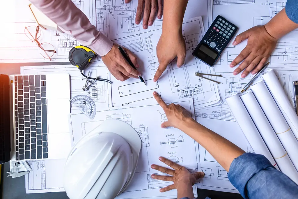 Les artisans d'un chantier calculent les besoins en materieaux devant un plan d'architecte.